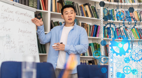 man standing next to a flipchart with words on it looking like he's talking to a class. He is standing in a library
